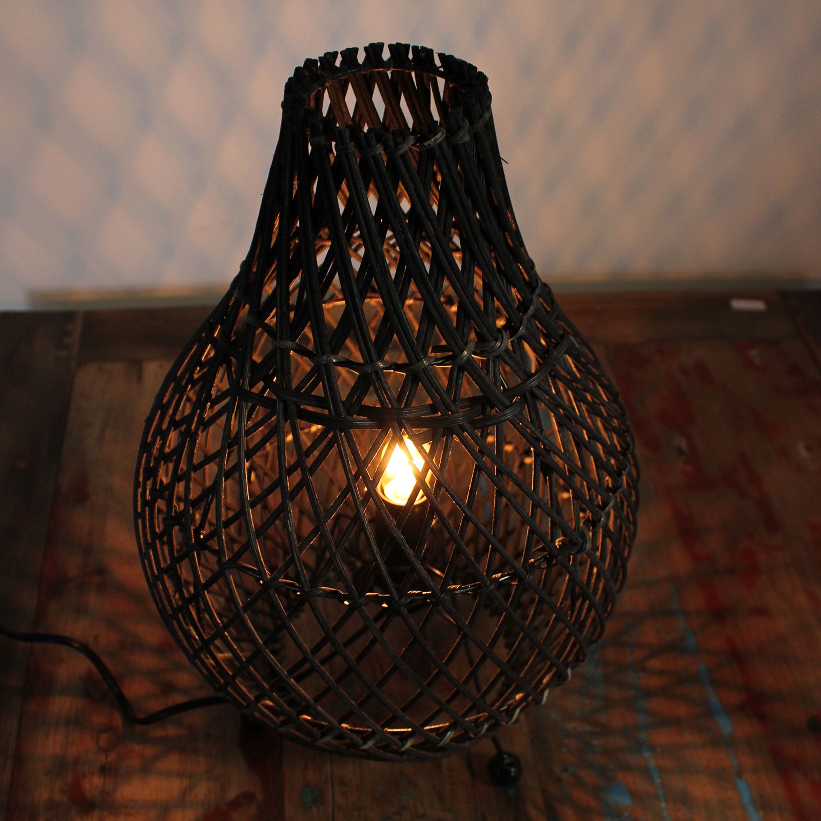 Woven rattan lamp with a lit bulb on a textured surface