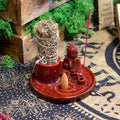 Red incense burner with Buddha figure and incense sticks on a patterned surface