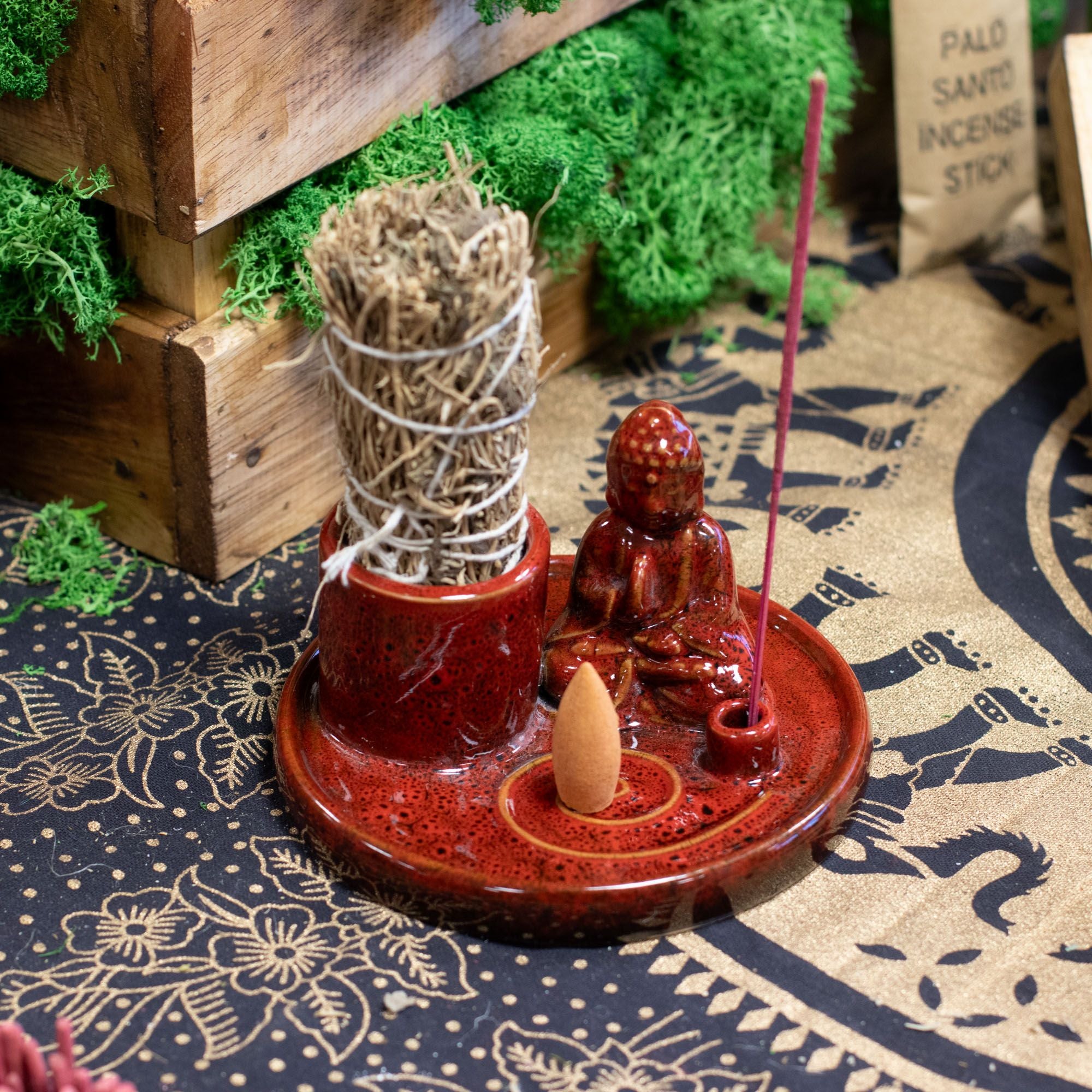 Red incense burner with Buddha figure and incense sticks on a patterned surface