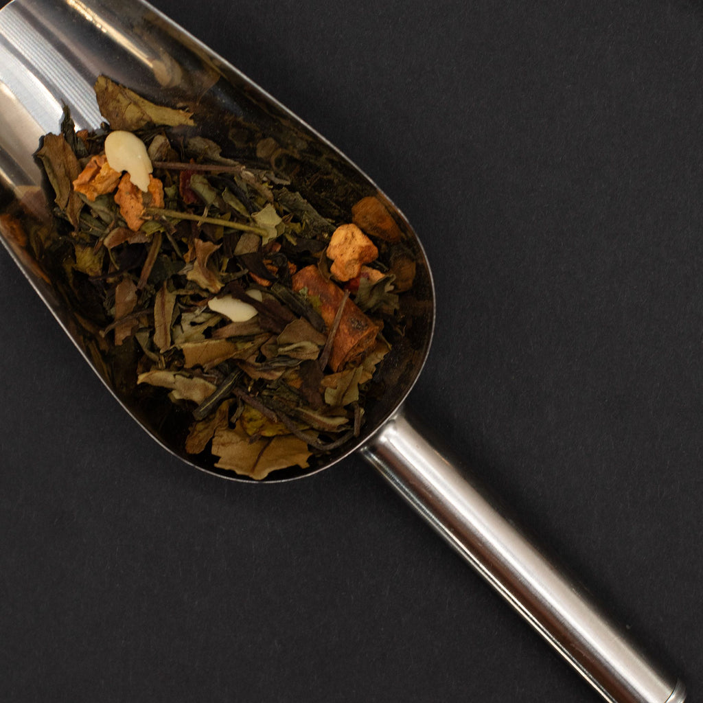 Metallic tea scoop filled with a mix of dried herbs and leaves on a black background