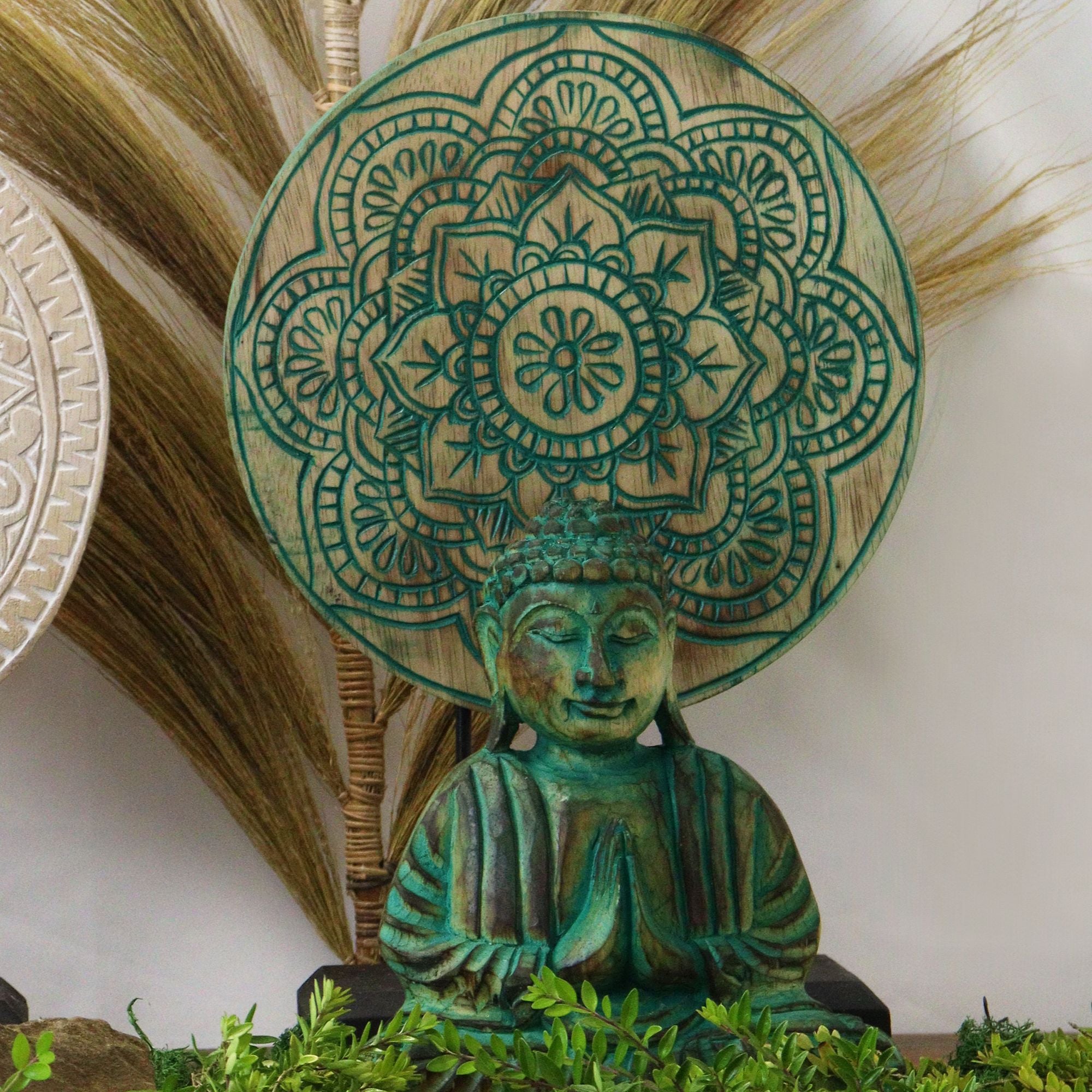 Decorative statue of a meditating figure with intricate green mandala design on head, surrounded by natural elements.