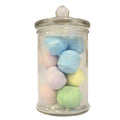 Glass jar filled with pastel-colored bath bombs on a white background