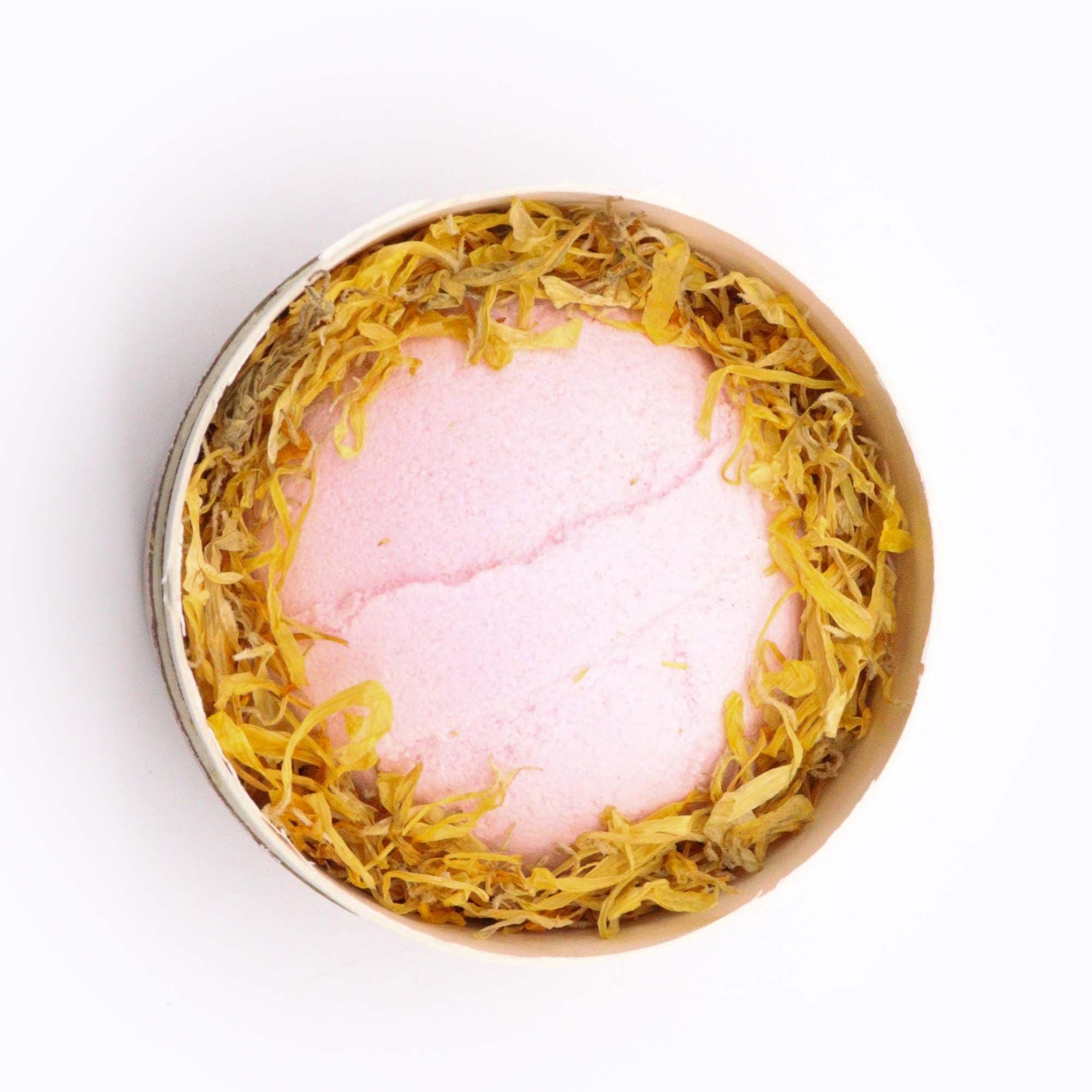 Pink bath bomb with gold leaf in a decorative container on a white background