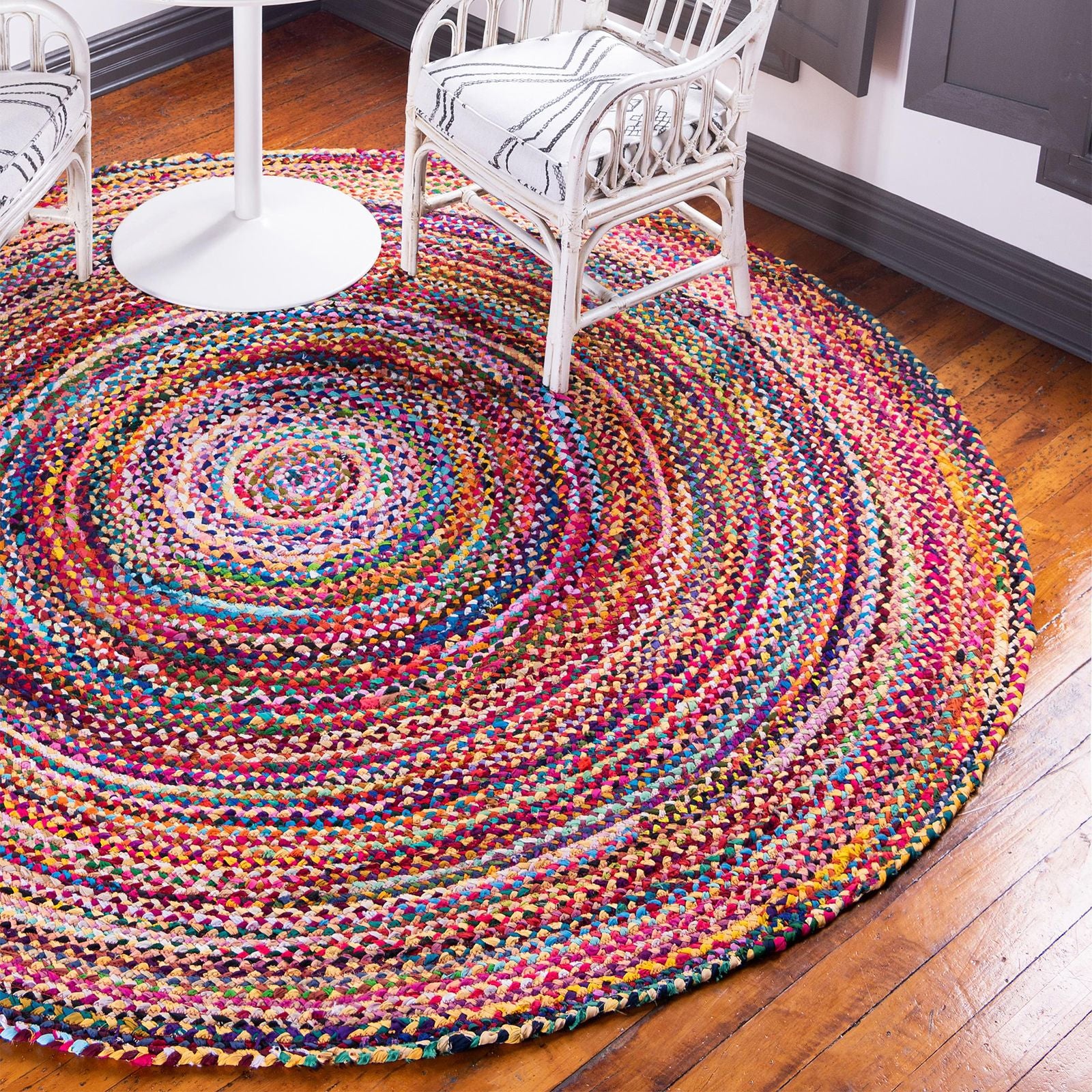 Multicolored braided rug on a wooden floor with white chairs.