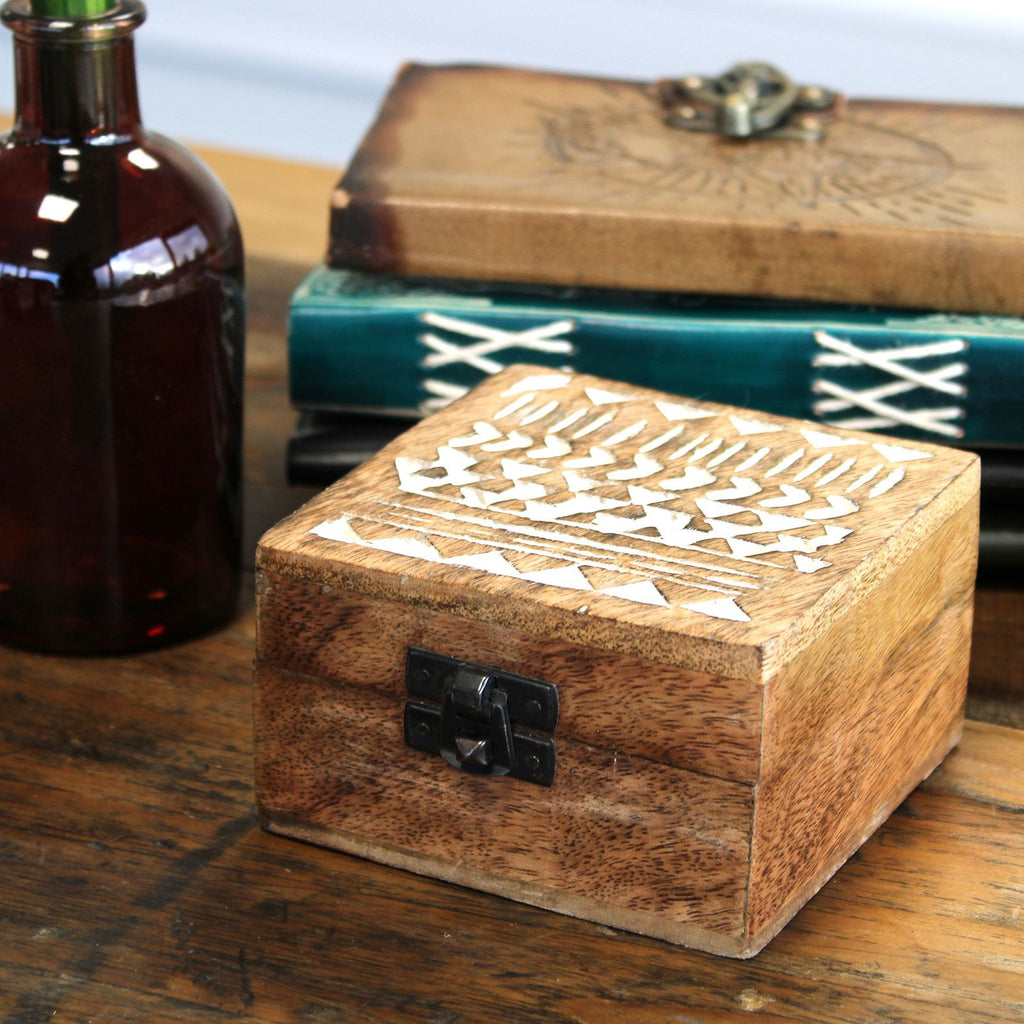 Wooden box with geometric patterns on a wooden surface with a bottle and books in the background.