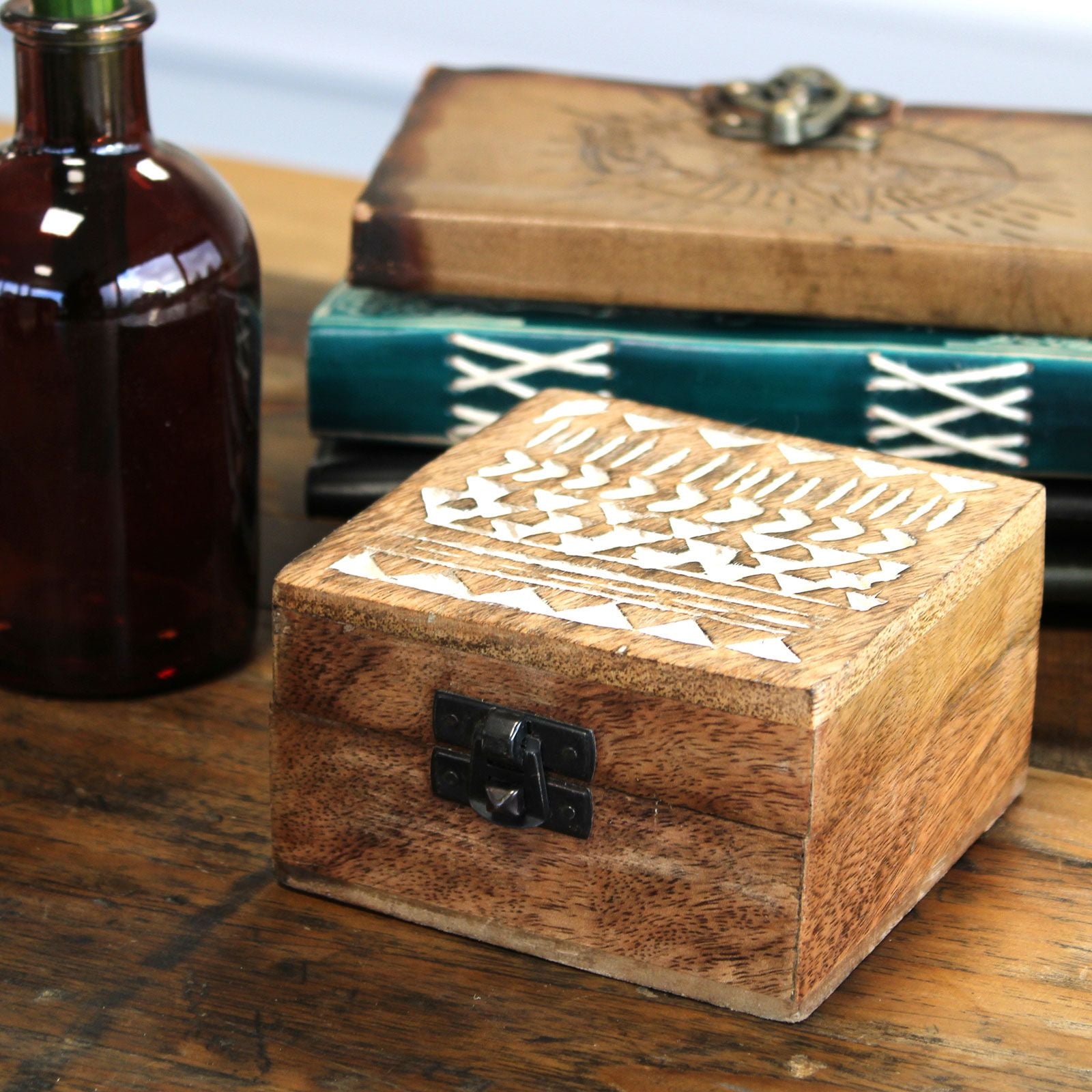 Wooden box with geometric patterns on a wooden surface with a bottle and books in the background.