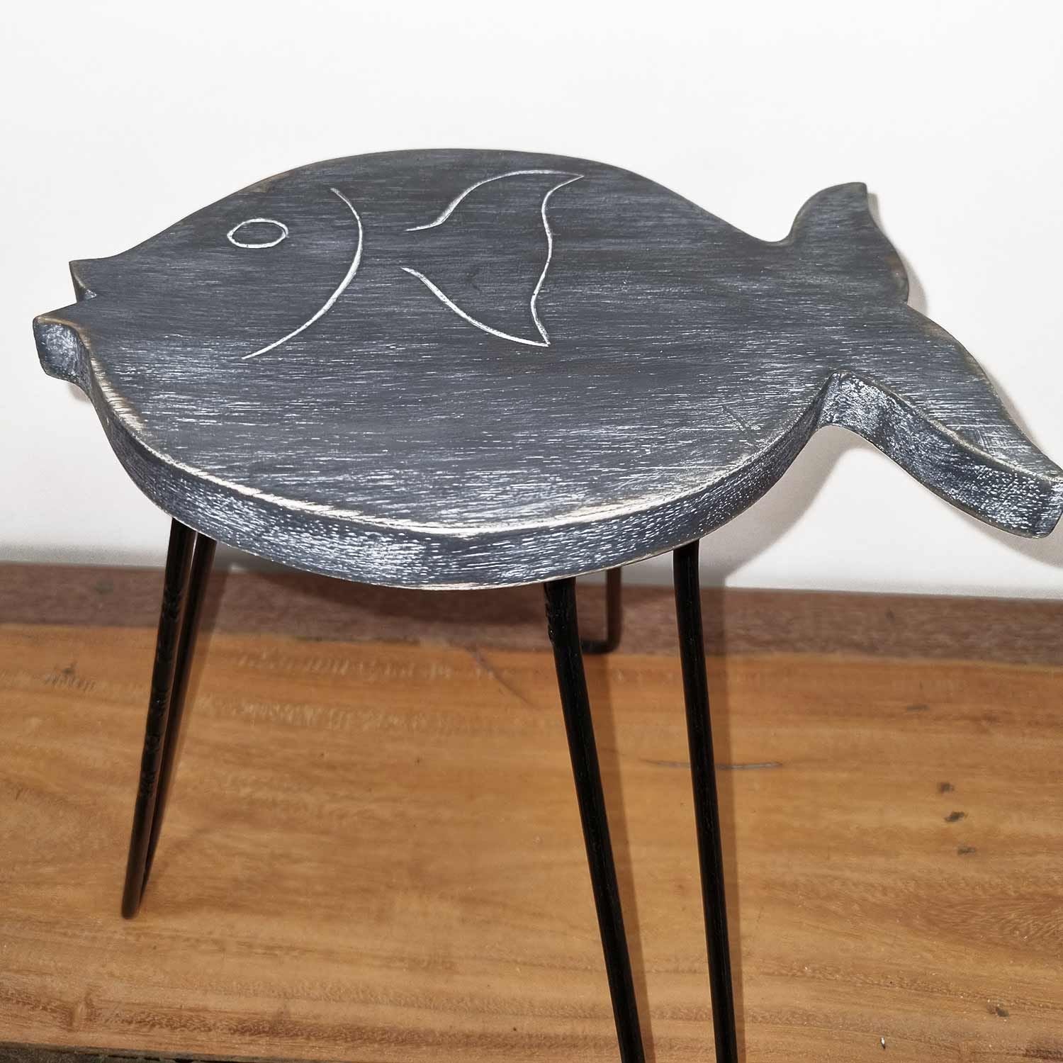Fish-shaped wooden stool with black legs on a wooden floor.
