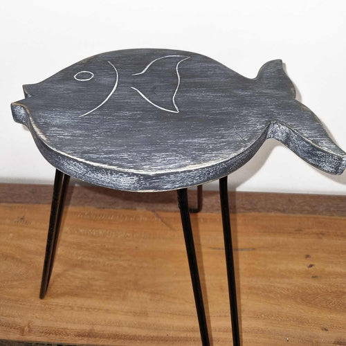 Fish-shaped wooden stool with black legs on a wooden floor.