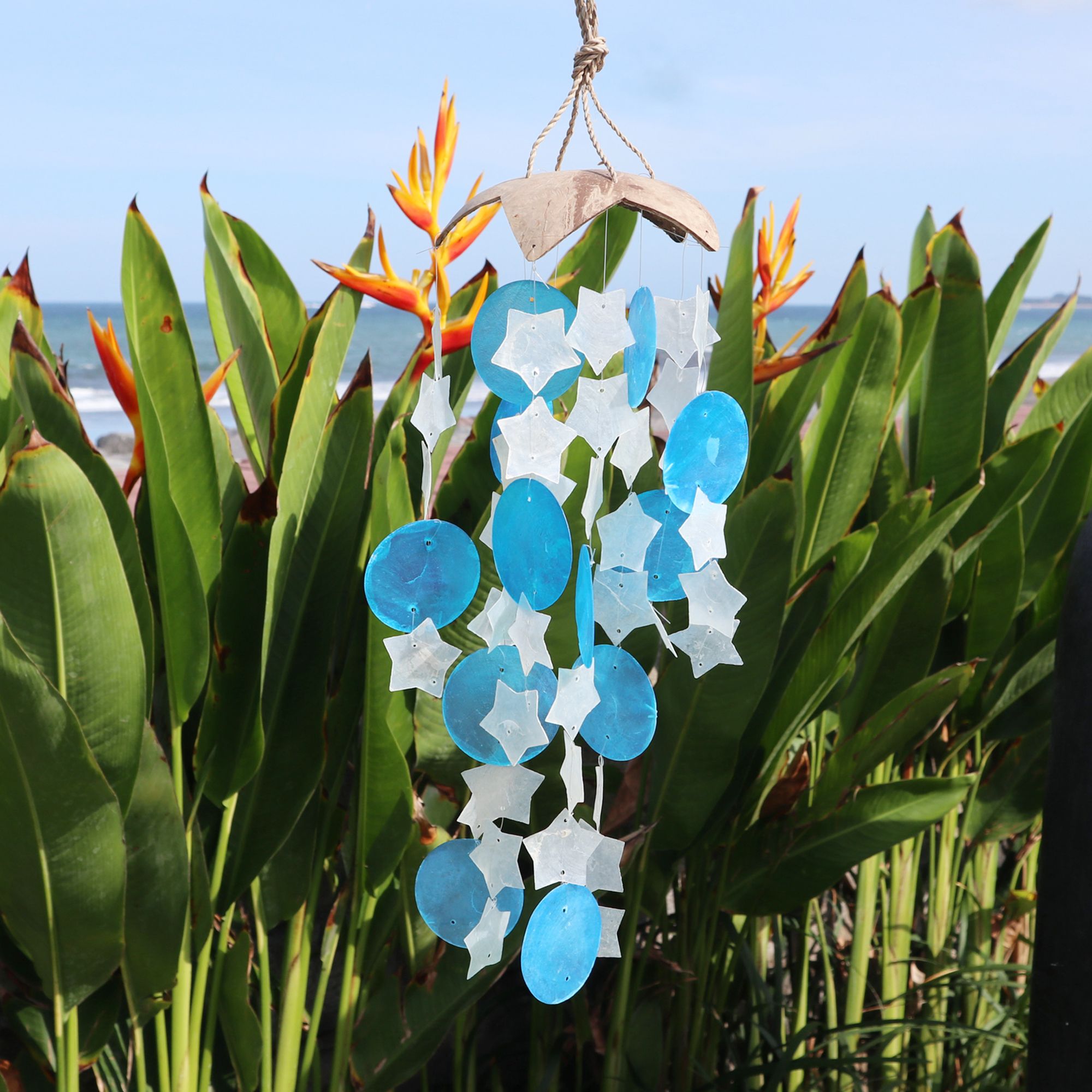 Decorative hanging with blue and white star shapes in front of tropical plants and ocean.
