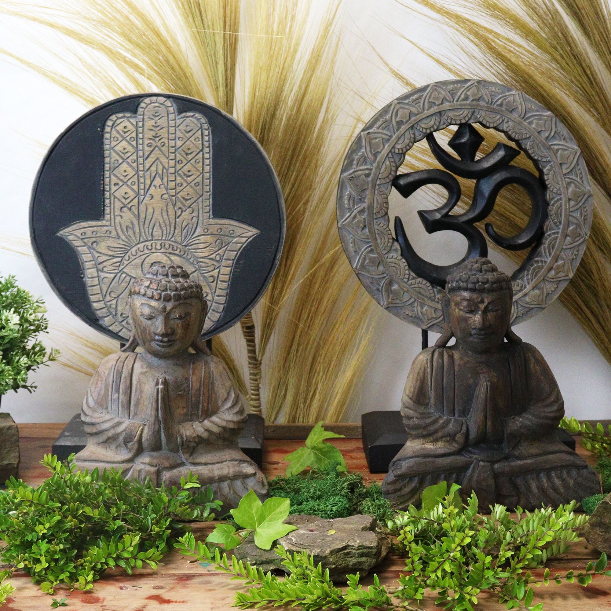 Two Buddha statues with Hamsa hand and Om symbol sculptures in a decorative setting with plants.
