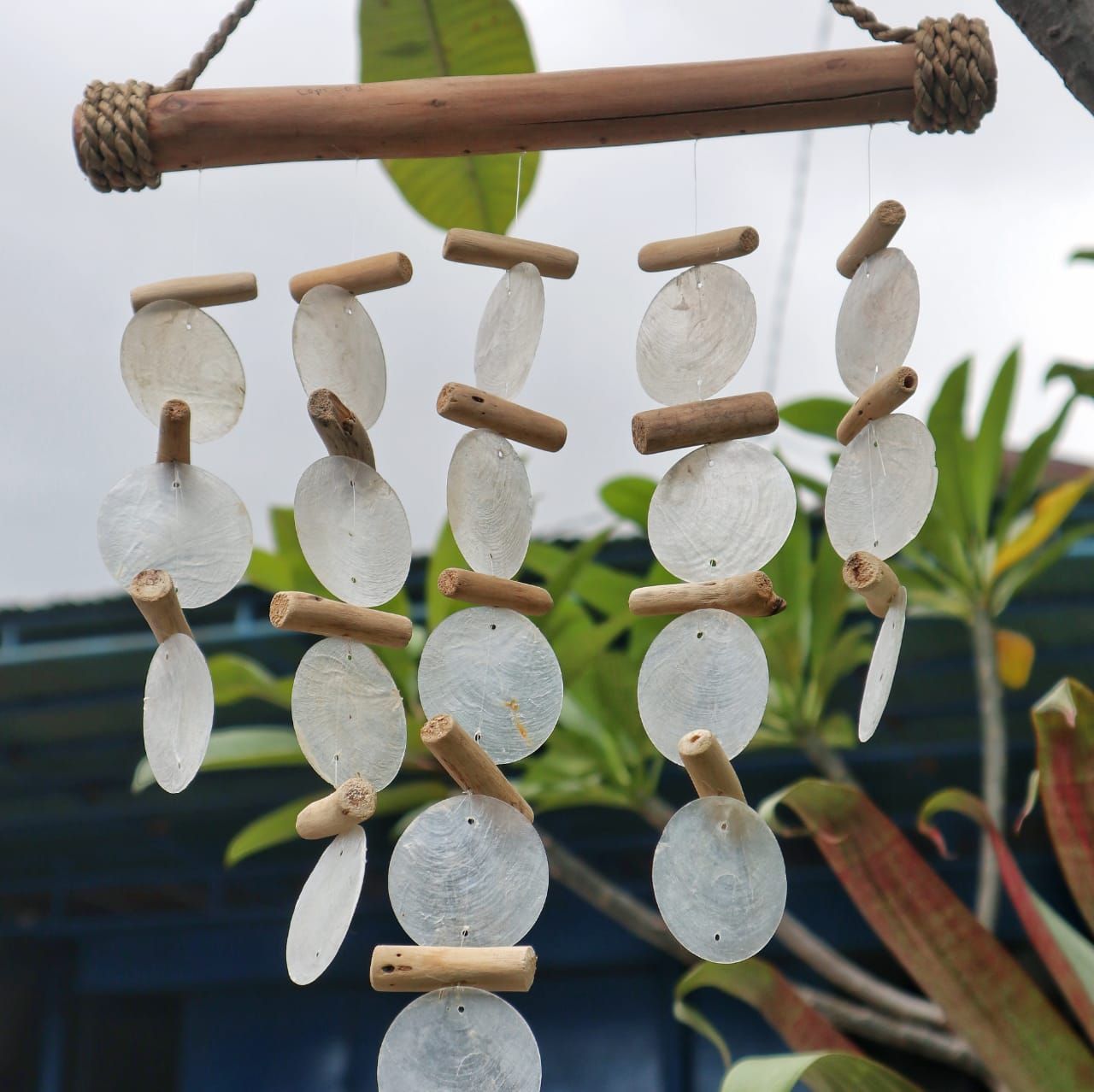 Decorative hanging with white stones and wooden sticks against a blurred natural background