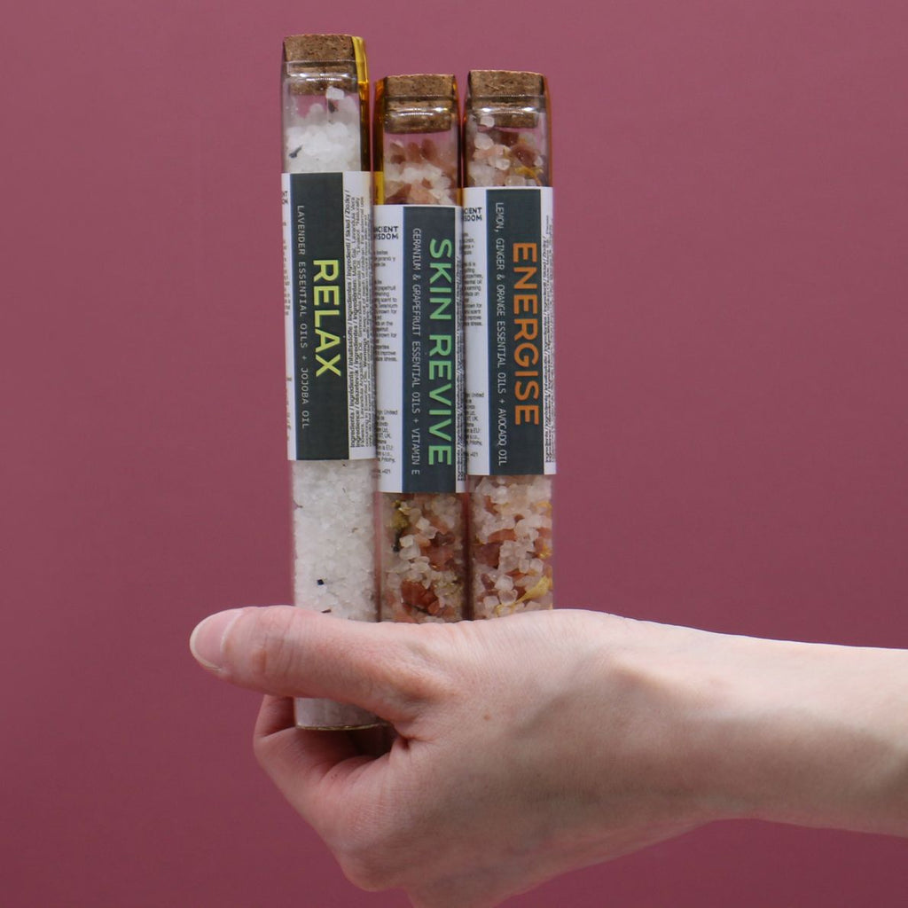 Hand holding three labeled wellness sticks against a pink background