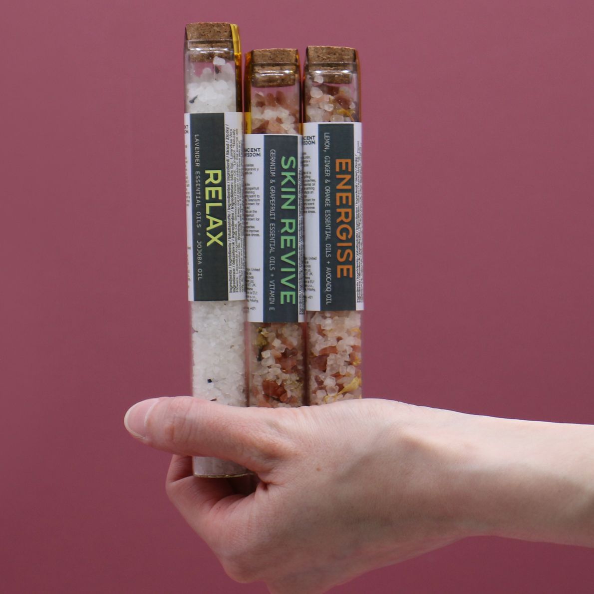 Hand holding three labeled wellness sticks against a pink background