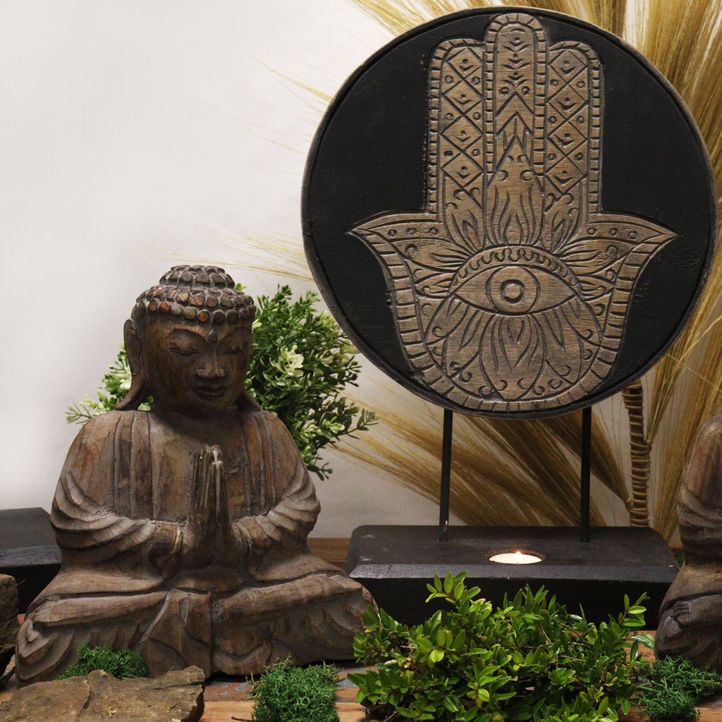 Decorative Hamsa hand with intricate patterns next to a Buddha statue and plants.