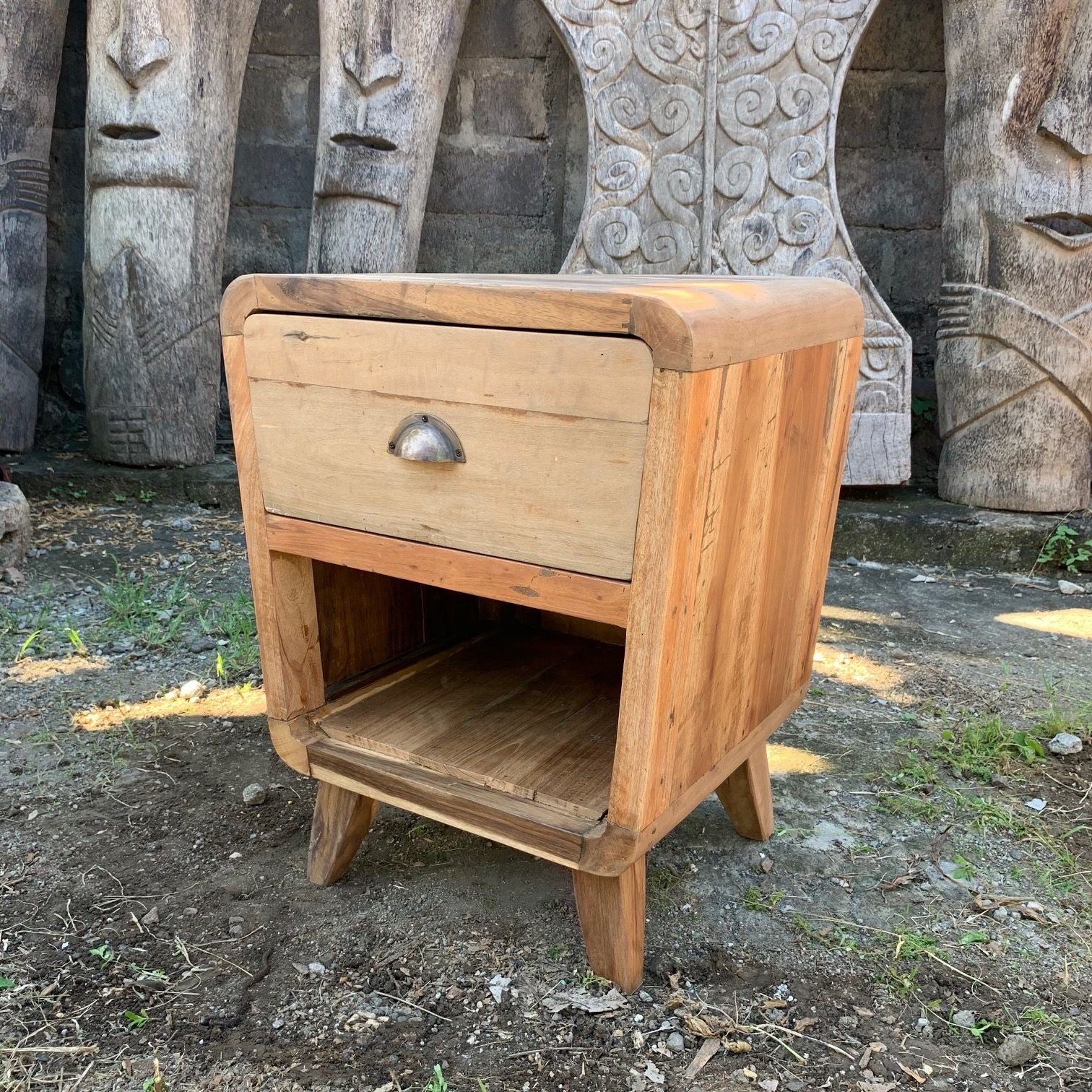 Wooden nightstand with a single drawer and open shelf against a stone wall background
