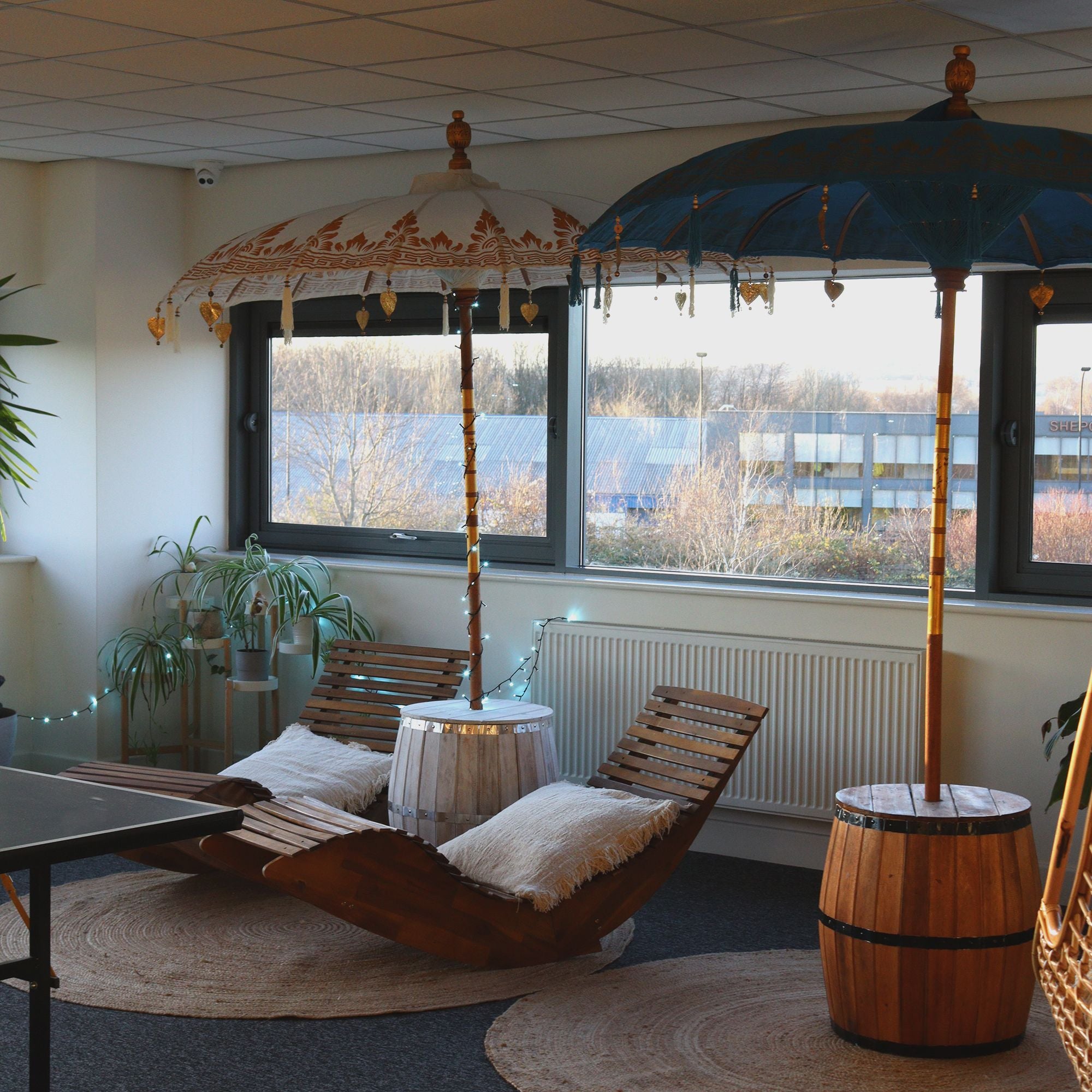 Modern interior with wooden lounge chairs, decorative umbrellas, and a view of trees outside.