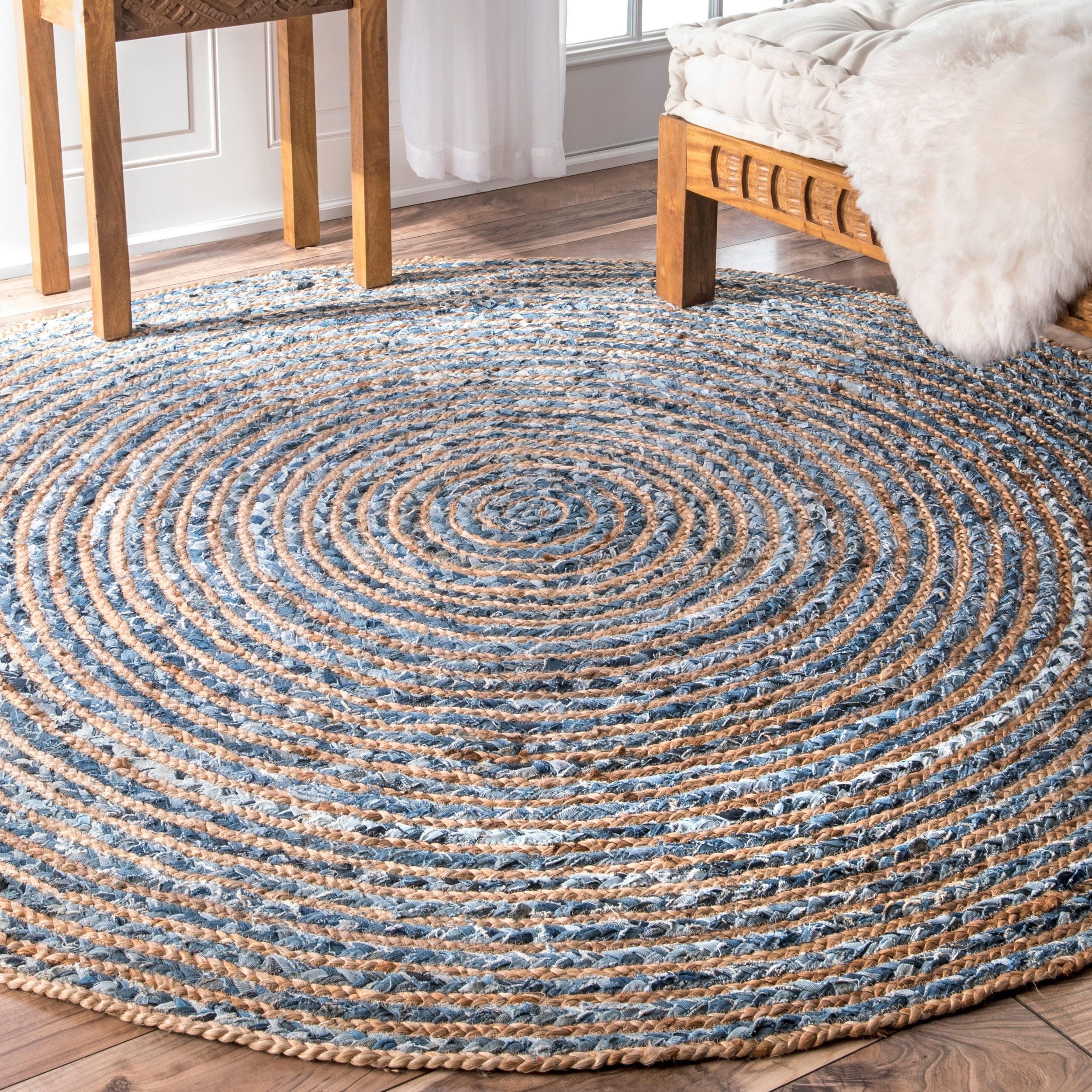 Round braided rug on a wooden floor with a wooden chair and bed in the background.