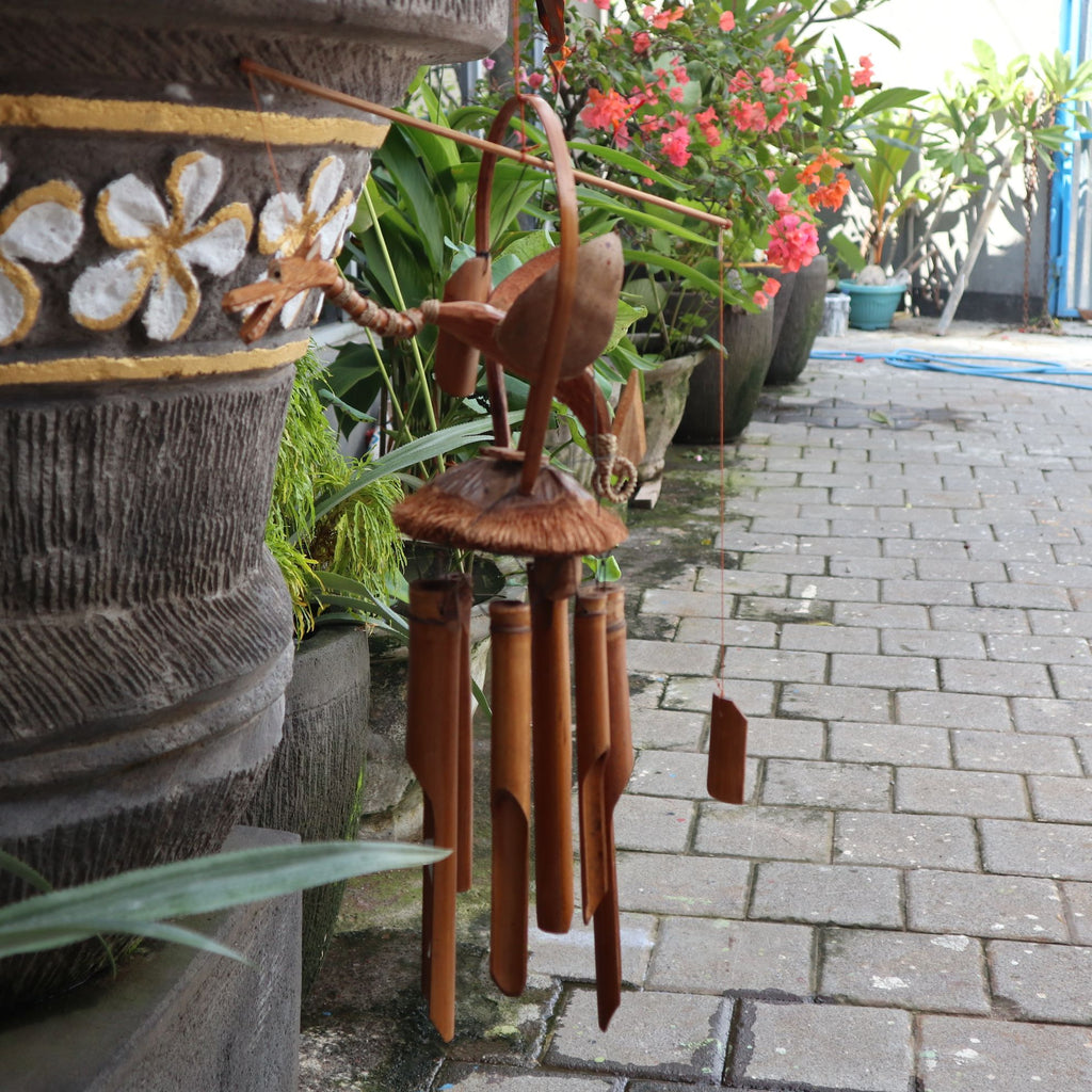 Wooden wind chime in front of decorative pots with plants on a stone path