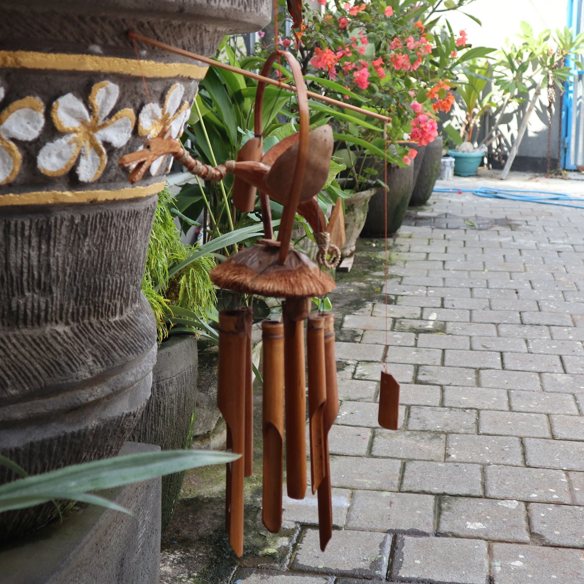 Wooden wind chime in front of decorative pots with plants on a stone path