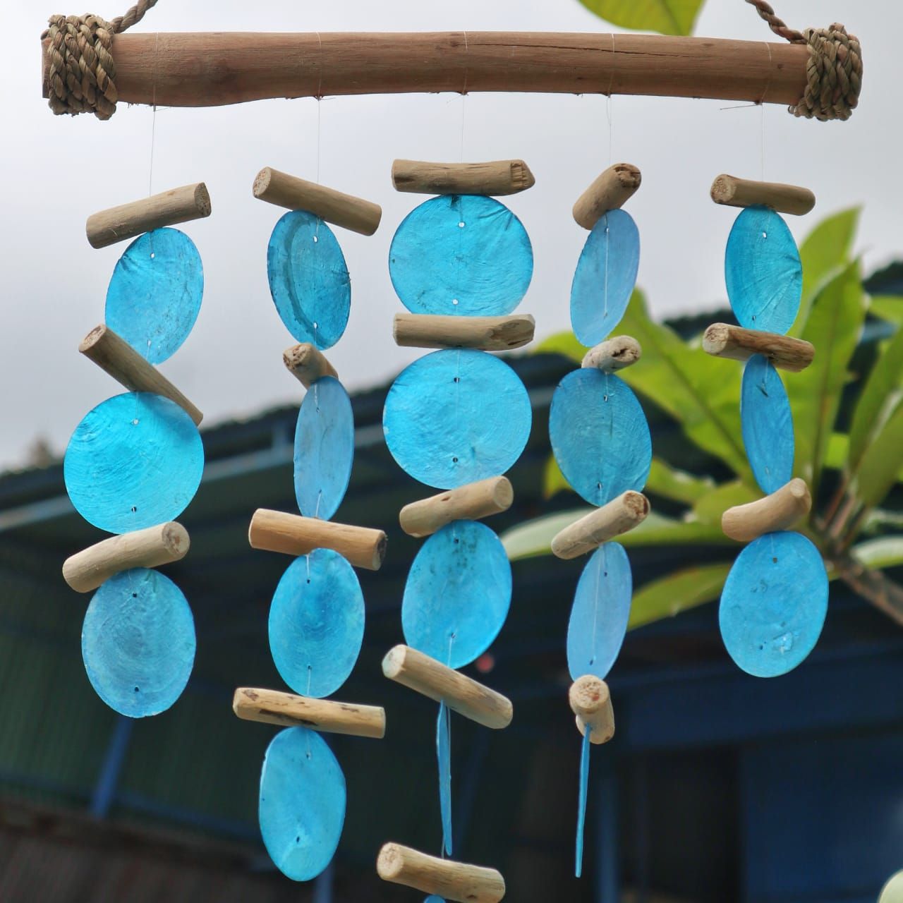 Decorative hanging with blue glass beads and wooden sticks against a blurred natural background