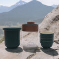Ceramic cups and a glass jar with wooden lid on a rock with mountain background