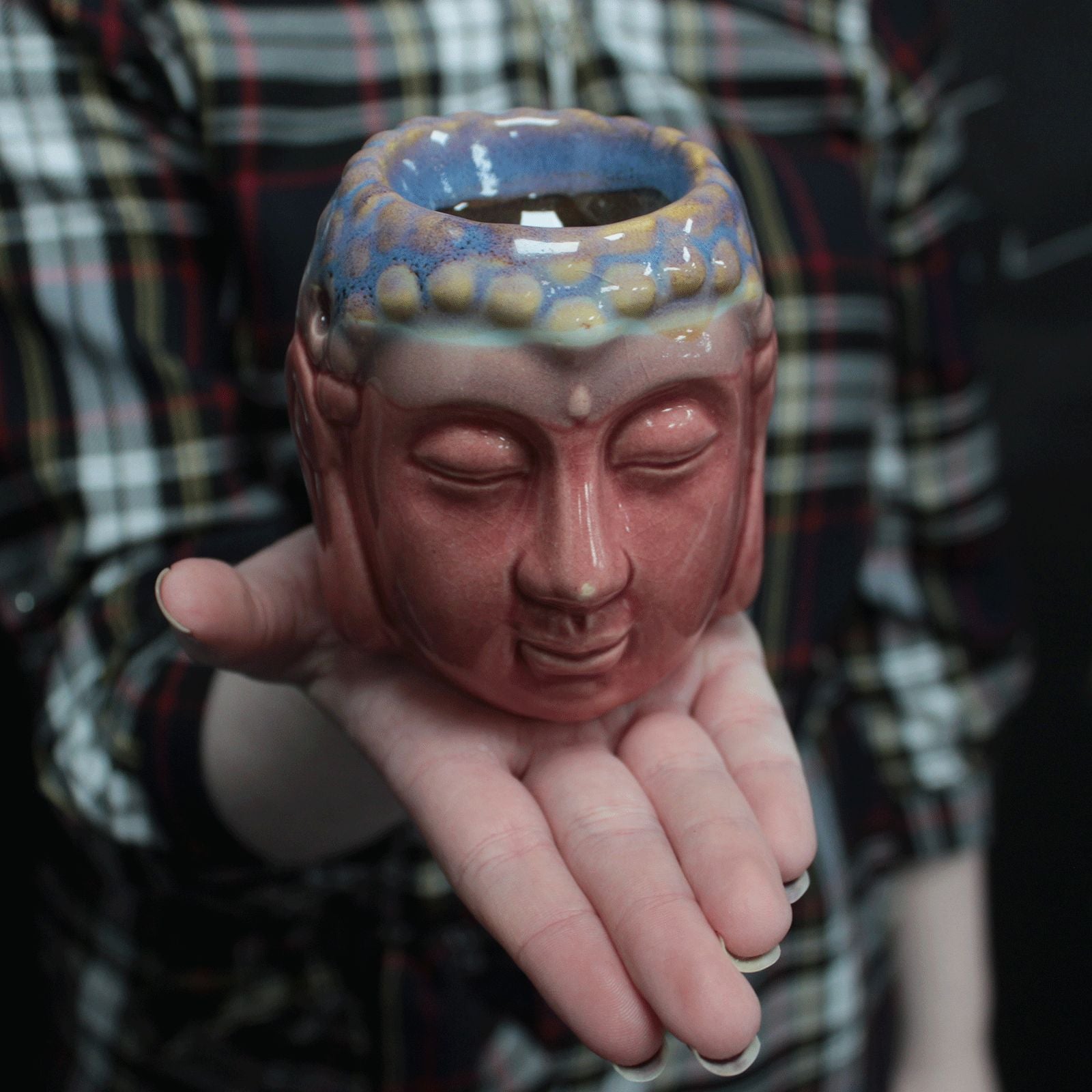 Ceramic Buddha head vase held in a hand with a blurred plaid shirt background