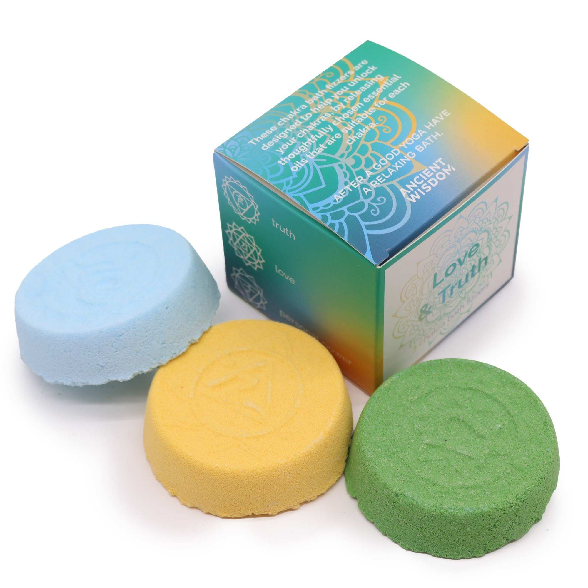 Three bath bombs in blue, yellow, and green with a box in the background on a white background