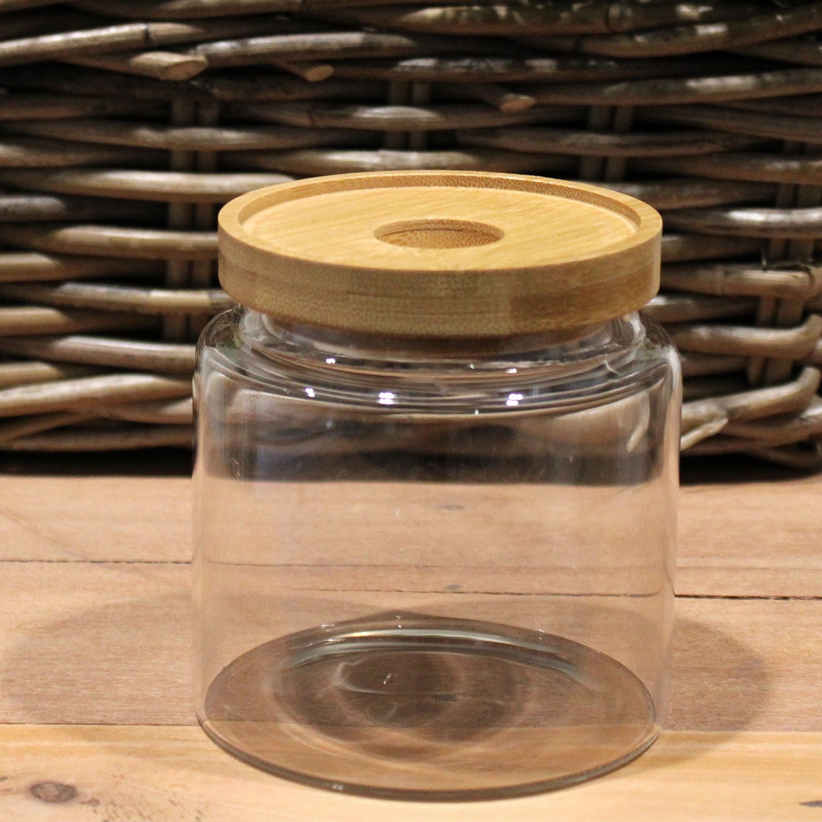 Clear glass jar with a wooden lid on a wooden surface with a wicker basket background