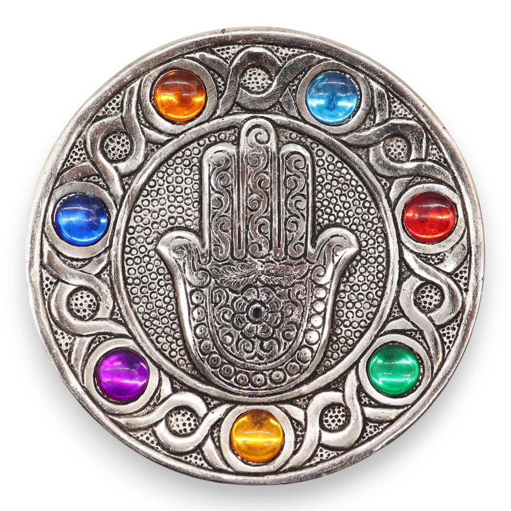 Circular metallic object with Hamsa hand design and colorful stones on a white background