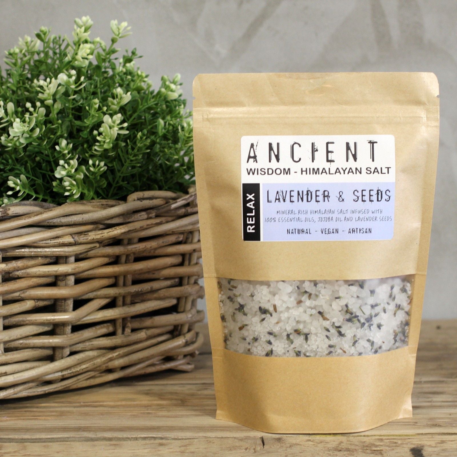 Bag of Himalayan salt with lavender and seeds on a wooden surface next to a basket of plants.