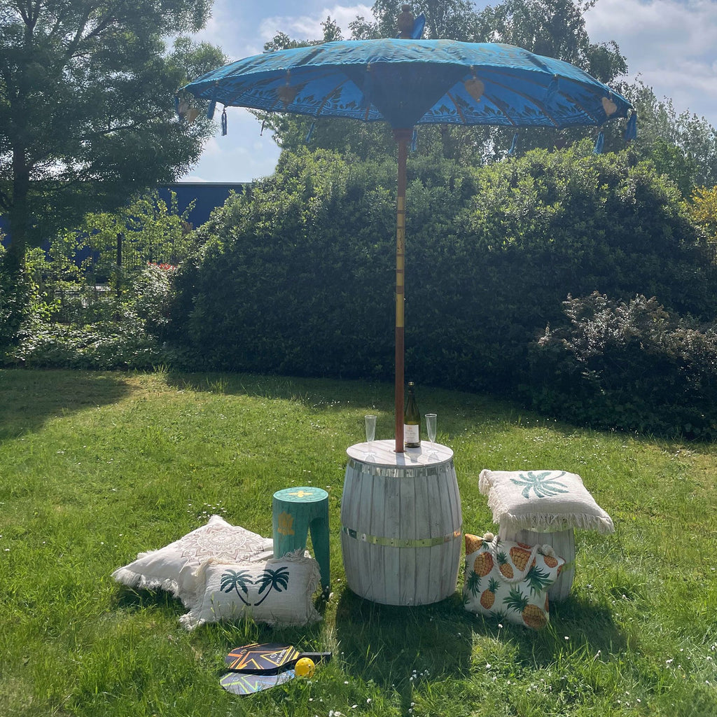 Outdoor setting with a blue umbrella, barrel table, and decorative items on grass.