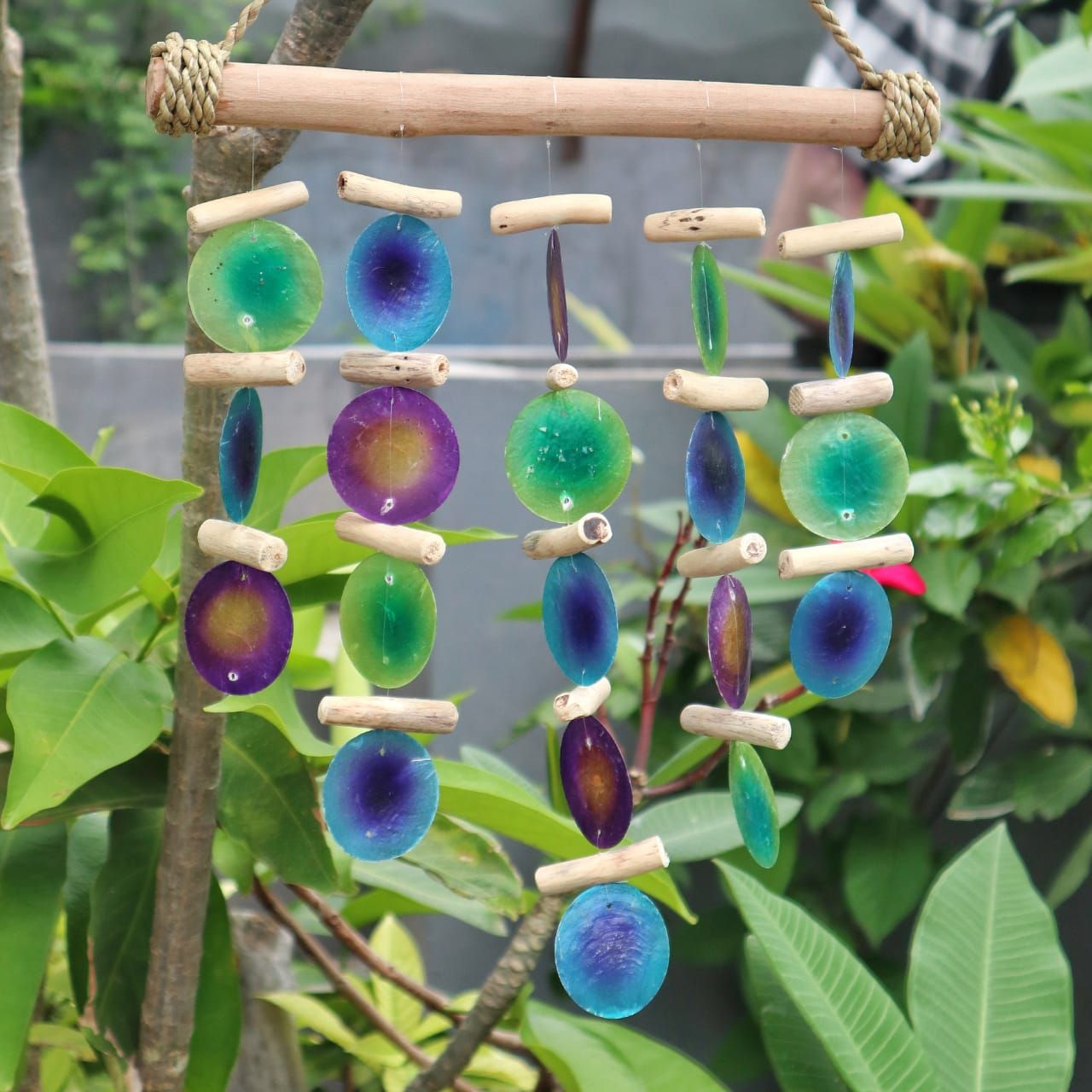 Colorful bead wind chime hanging among green leaves