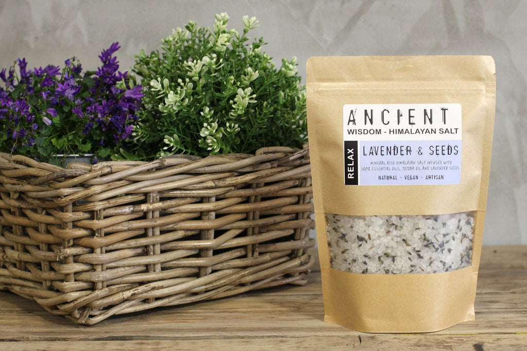 Bag of Himalayan salt with lavender and seeds next to a woven basket with plants on a wooden surface.