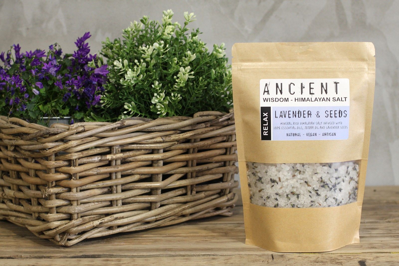 Bag of Himalayan salt with lavender and seeds next to a woven basket with plants on a wooden surface.