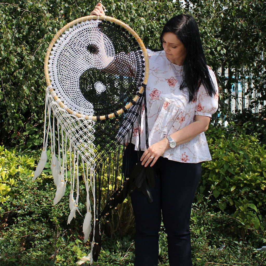 Woman holding a large dreamcatcher with a yin and yang symbol against a green outdoor background.