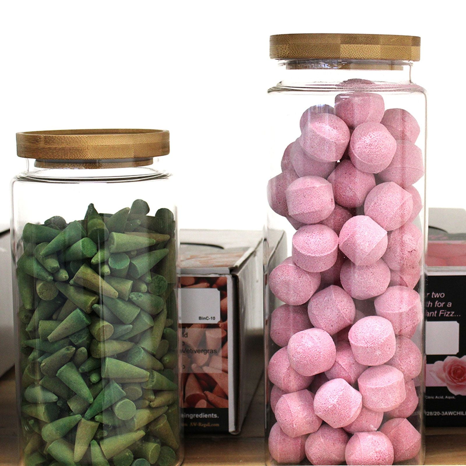 Two glass jars with wooden lids, one containing green candy and the other pink candy, on a white background.